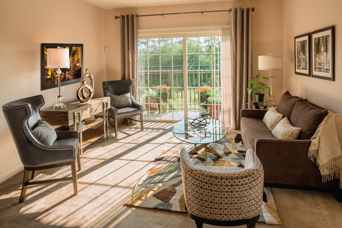 A cozy, well-lit living room with stylish furniture and a view through sliding glass doors.
