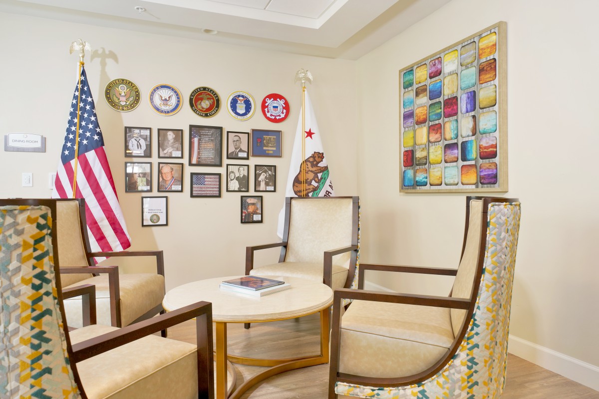 A small office conference room featuring a round table, several chairs, an American flag, and military plaques on the wall.