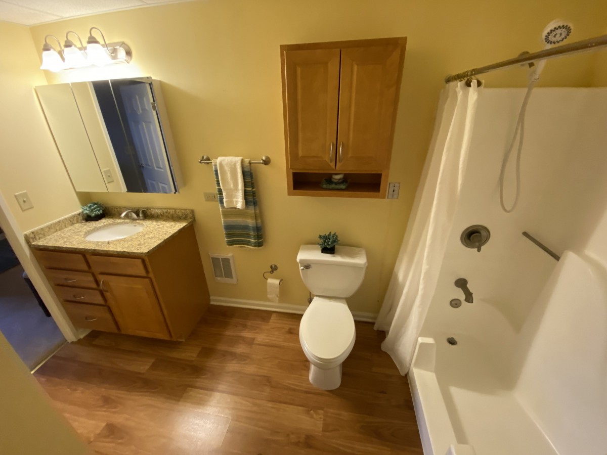 A well-organized bathroom with a bathtub, sink, toilet, and wooden flooring.