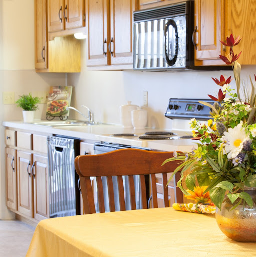 A cozy kitchen featuring wooden cabinets, modern appliances, and a dining table adorned with a vibrant flower arrangement.