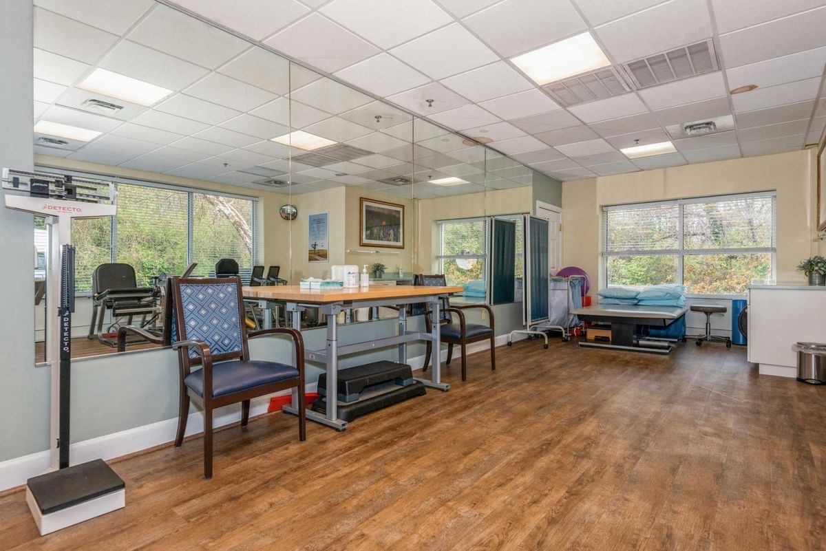 An office waiting area with chairs, a table, and large windows providing natural light.