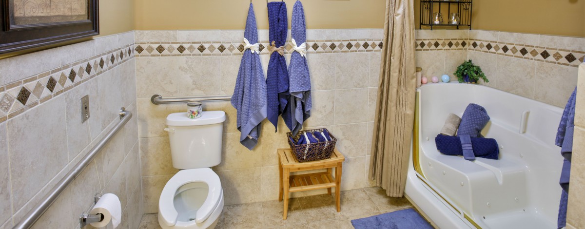 A bathroom with blue towels hanging, a toilet, and a wooden stool holding a basket.