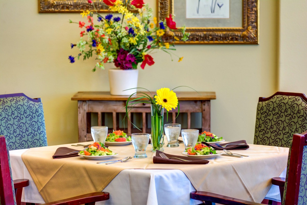 A beautifully set dining table adorned with salads and colorful flowers.