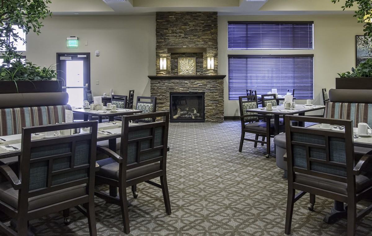 A cozy dining room with multiple tables and chairs, featuring a stone fireplace.