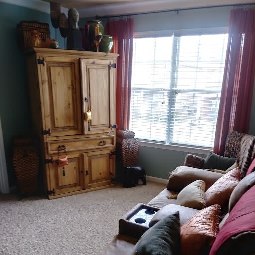 A cozy living room with a large couch, wooden armoire, and natural light coming through the window.