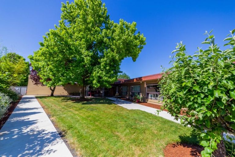 A sunny day with a view of a building surrounded by lush green trees and a well-maintained lawn.
