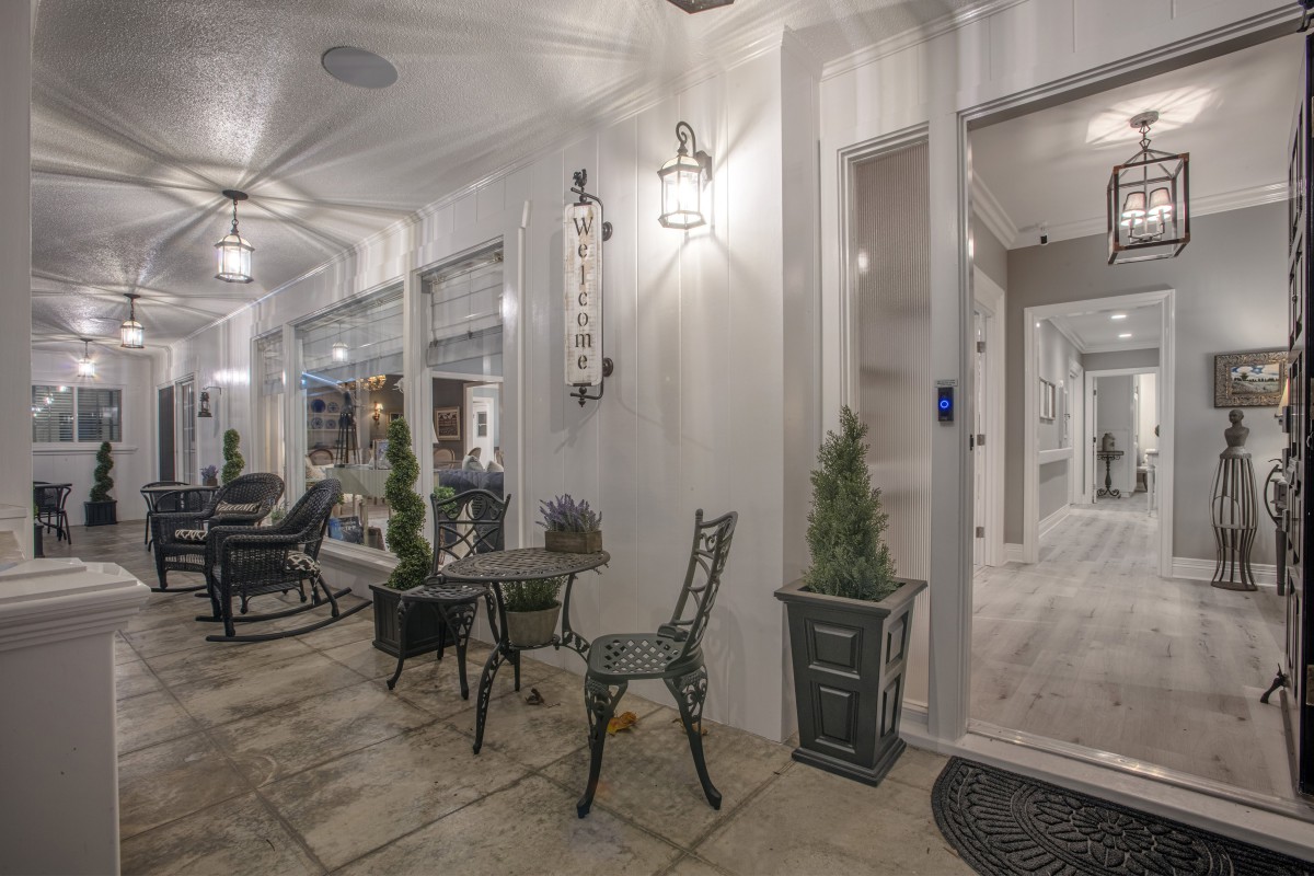 A cozy porch area with chairs, a table, and decorative plants illuminated by soft lighting.