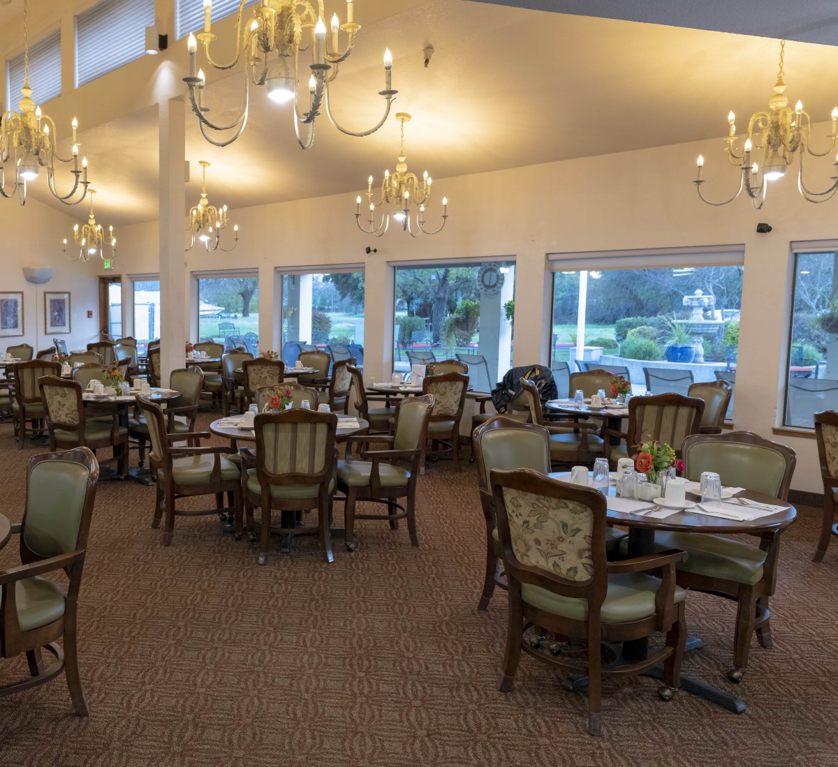 An elegant dining room with chandeliers and classic furniture arranged around set tables.