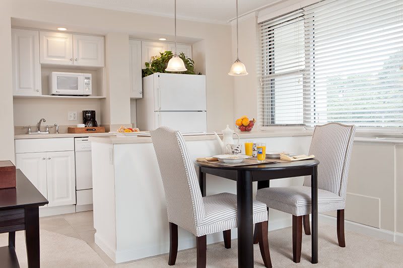 A modern kitchen and dining area with white furniture and ample natural light.