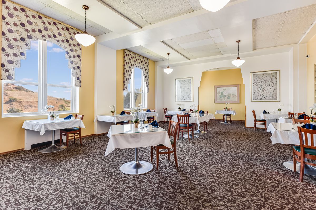An elegant dining room with neatly arranged tables and chairs, featuring large windows and sophisticated decor.