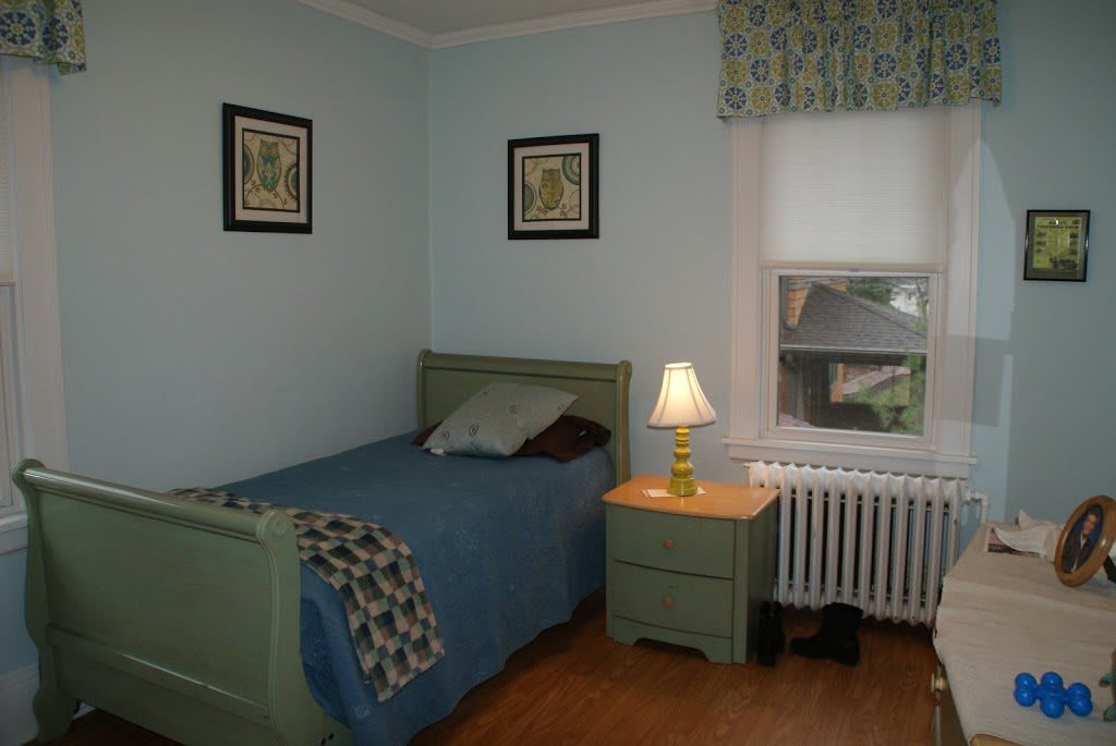 A cozy bedroom with a single bed, nightstand, and lamp near a window.