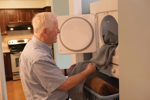 An elderly person doing laundry, loading clothes into a dryer.