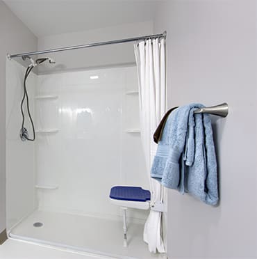 A minimalist bathroom with a walk-in shower featuring a blue shower seat and neatly hung towels.