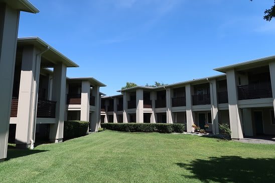 A modern apartment complex with a central grassy courtyard under a clear blue sky.