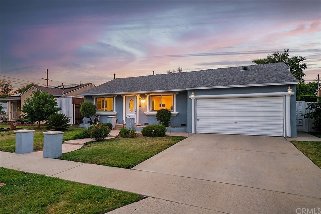 A cozy suburban house with a well-maintained lawn and driveway, illuminated at dusk.