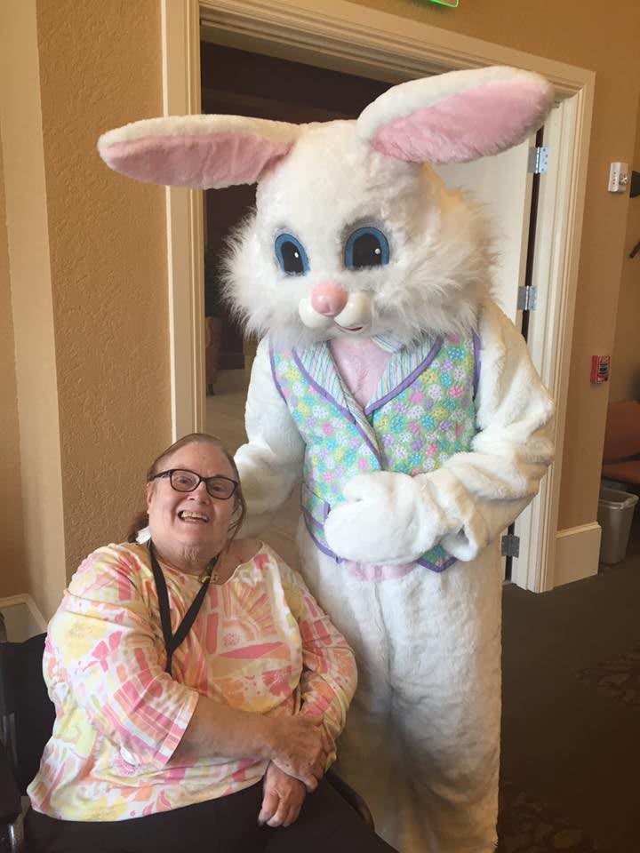 A person sitting next to someone dressed in an Easter Bunny costume indoors.