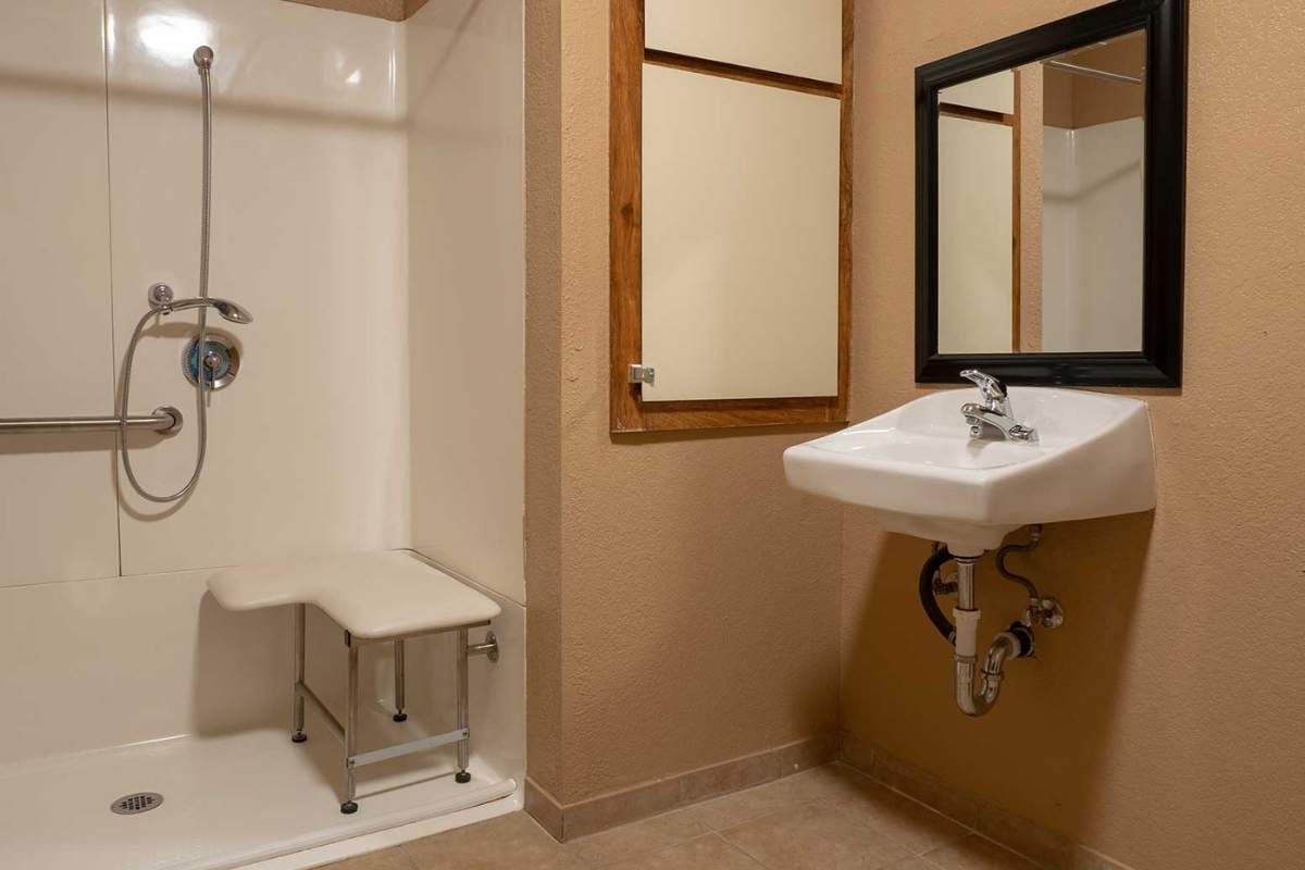 An accessible bathroom with a wall-mounted sink and shower equipped with a seating area.