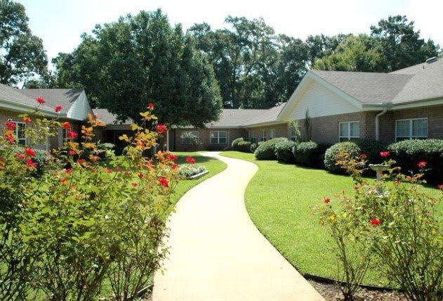 A serene garden walkway lined with vibrant flowers and neatly trimmed hedges leading to a house.