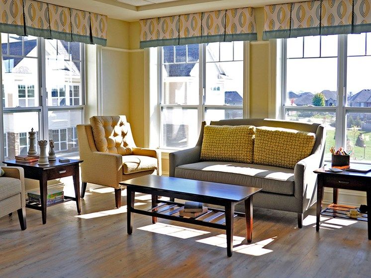 A cozy living room with sunlit windows, featuring a sofa, armchair, and coffee table.