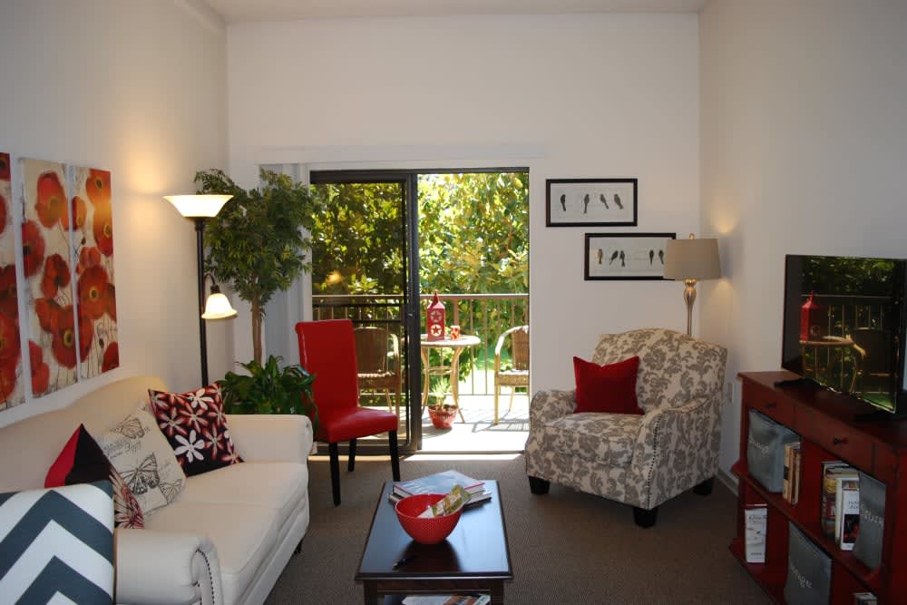 A cozy living room with bright furniture, plants, and a view of the balcony.
