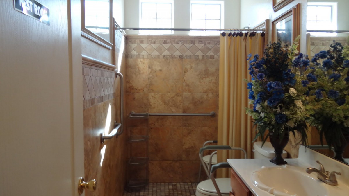 A small bathroom featuring a shower with patterned tiles, a yellow curtain, and blue floral decorations on the sink counter.