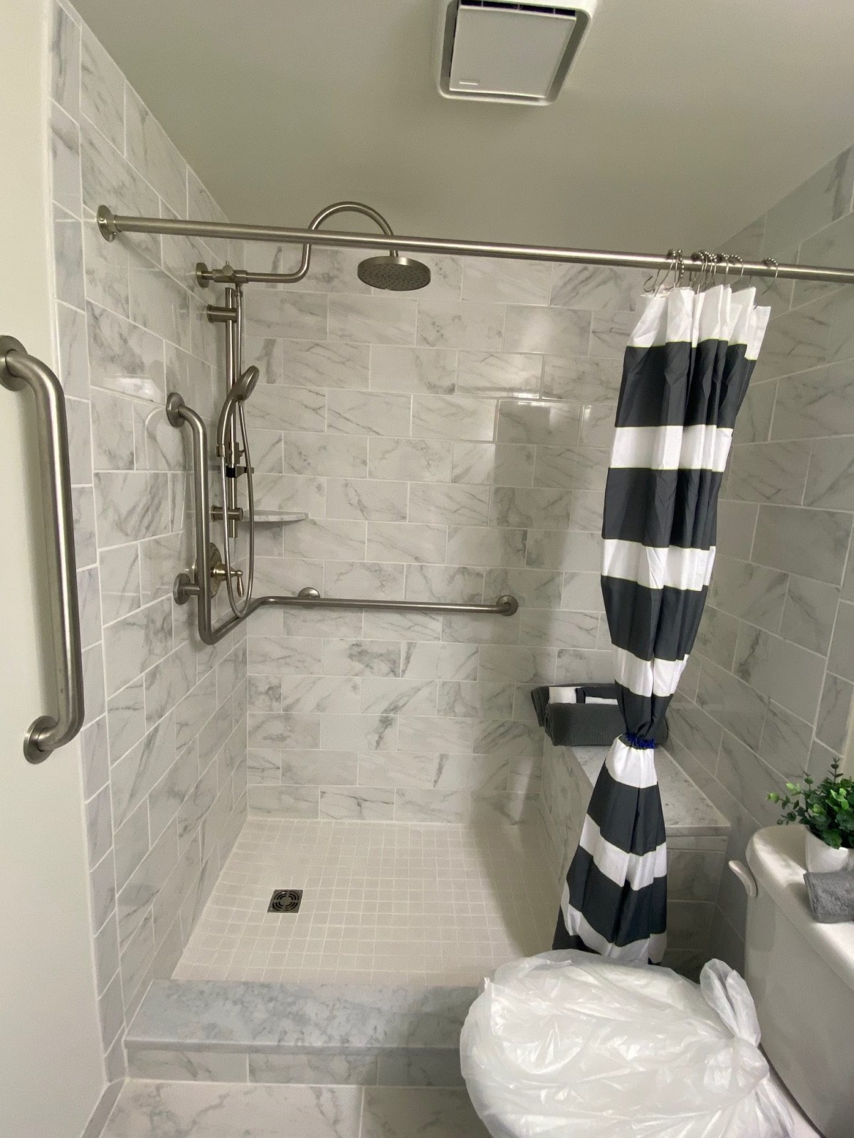 A modern bathroom featuring a tiled shower with a striped curtain and safety grab bars.