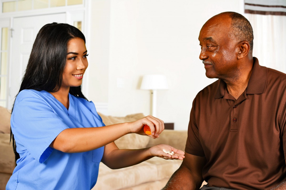 A healthcare professional assisting an elderly man with medication.