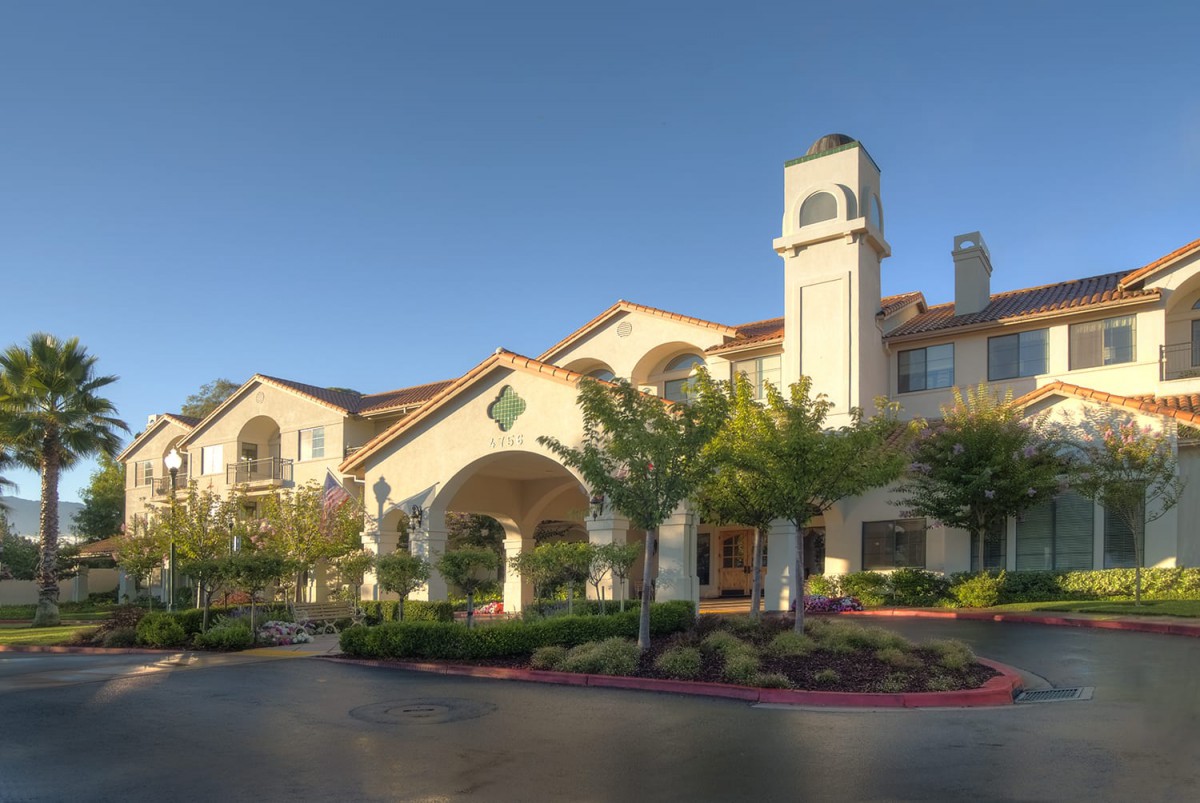A beautiful residential building with Mediterranean-style architecture surrounded by landscaped greenery under a clear blue sky.