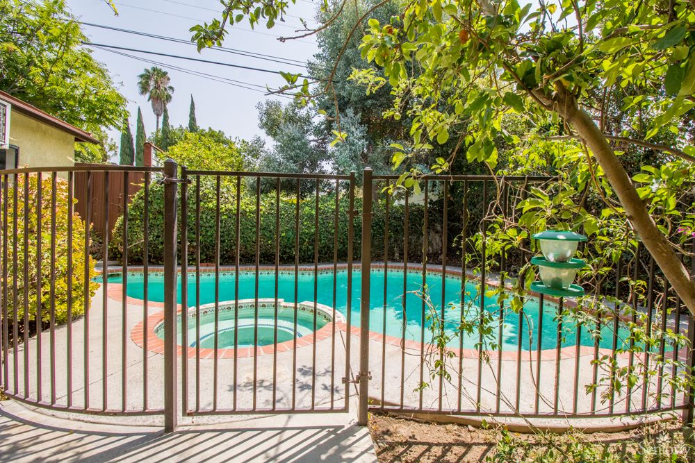 A fenced backyard pool surrounded by trees on a sunny day.