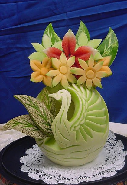 A beautifully carved fruit sculpture featuring a swan, flowers, and leaves.