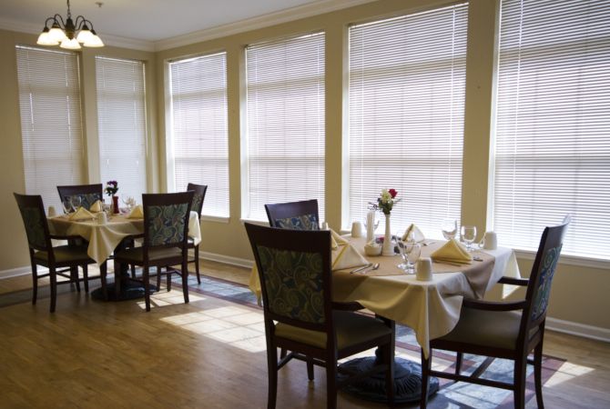 A cozy dining room with neatly arranged tables and chairs, bathed in sunlight.
