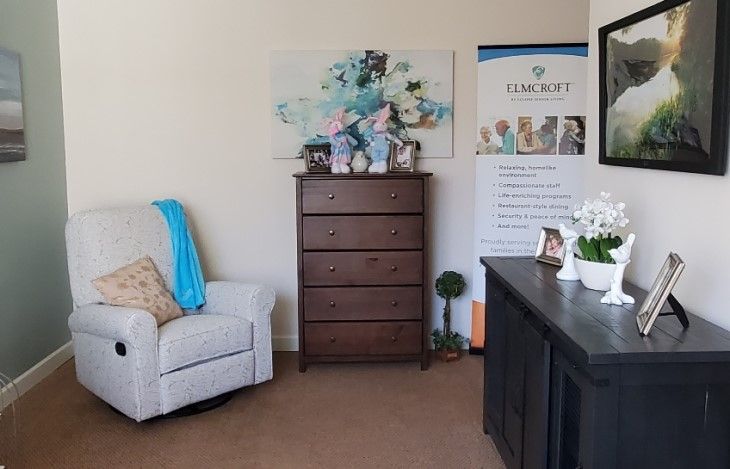 A cozy office space with a chair, dresser, and desk featuring decorative items and artwork.