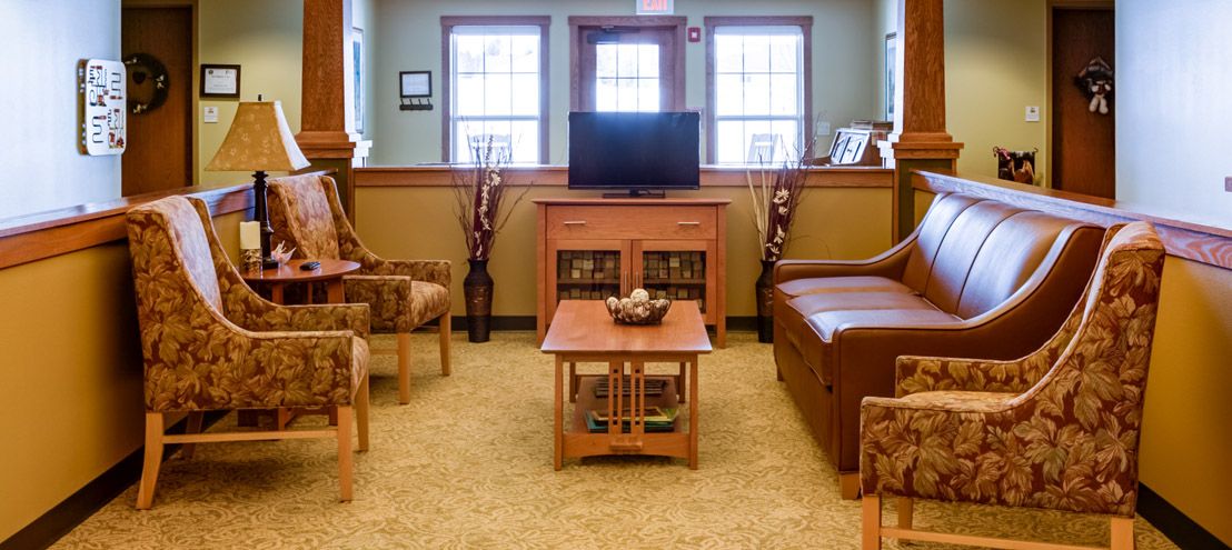 A cozy living room with a television, sofa, chairs, and a coffee table in front of two windows.