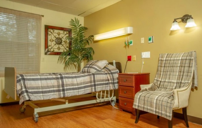 A cozy hospital room with a bed, chair, and warm decor.