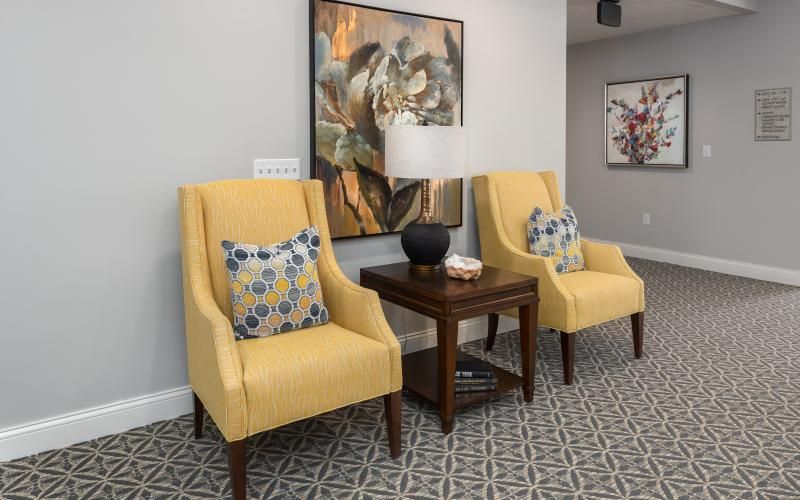 A cozy seating area with yellow chairs and a side table, adorned with a lamp and artwork.