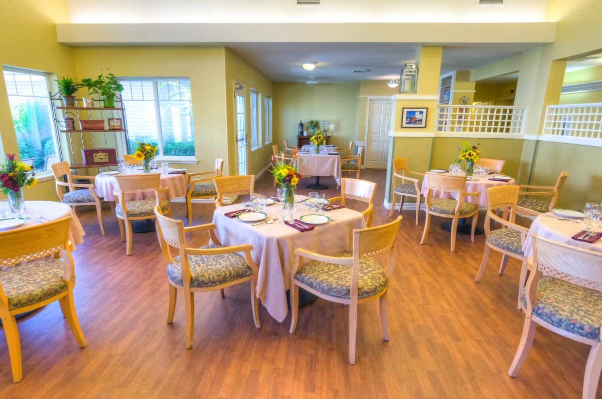 A well-lit dining area with neatly arranged tables and chairs, featuring wooden floors and decorative elements.
