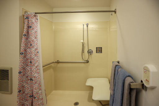 An accessible shower featuring grab bars, a shower seat, and towels neatly hanging.