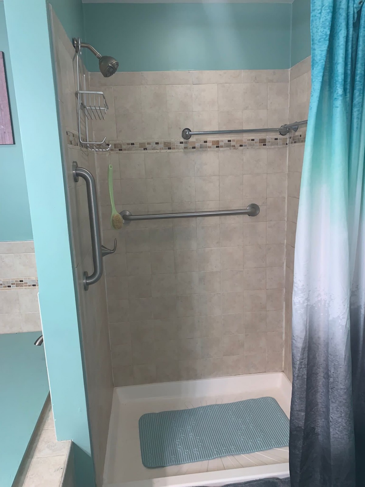 A bathroom featuring a tiled shower with grab bars and a gradient shower curtain.