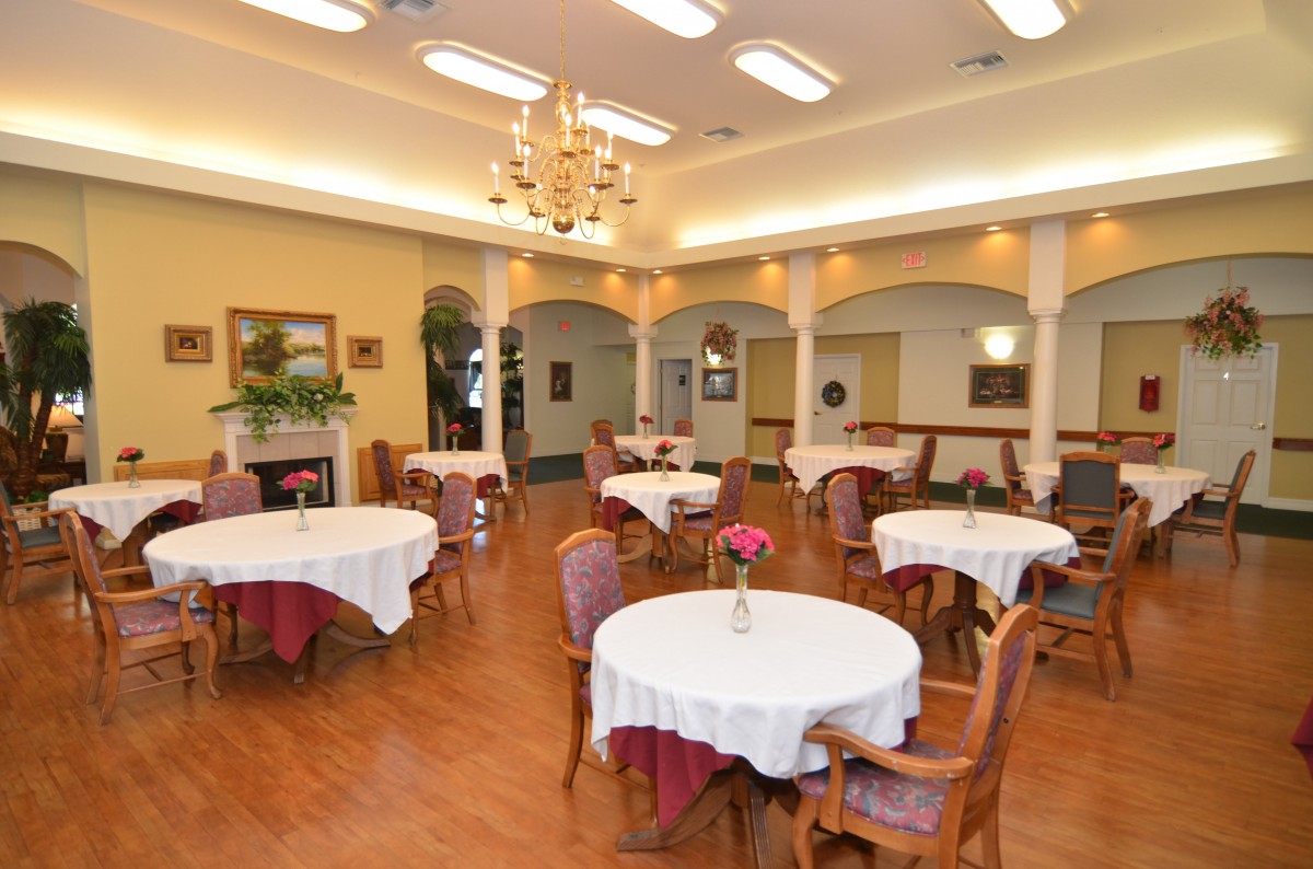 An elegant dining area with round tables, white tablecloths, and a central chandelier.