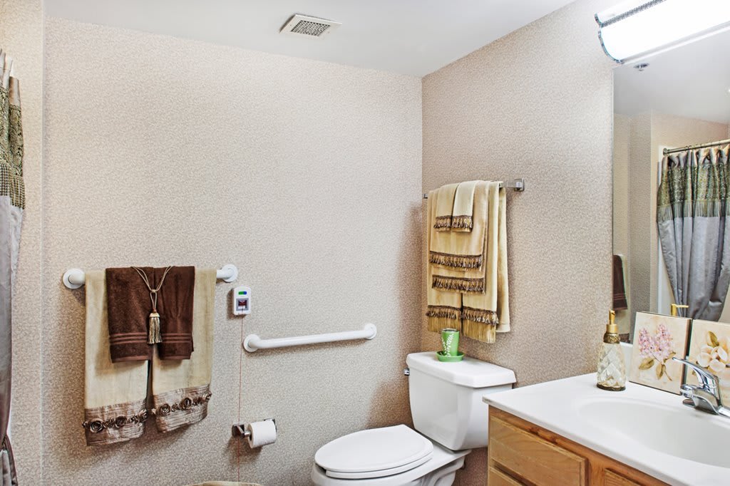 A well-organized bathroom with a toilet, sink, towels, and safety grab bar.