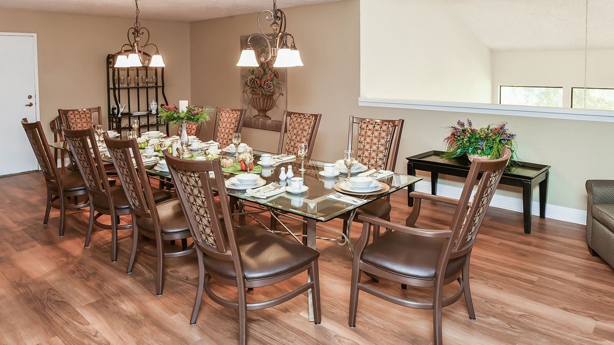 A beautifully arranged dining room with a glass table set for a meal, surrounded by elegant chairs and illuminated by a chandelier.