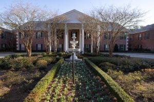 A grand mansion with a prominent fountain and landscaped garden in the foreground.