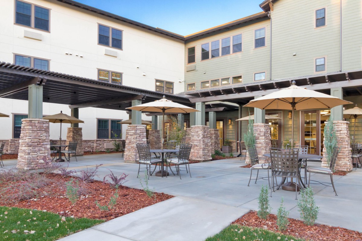 A modern outdoor patio area with tables and umbrellas in front of a multi-story building.