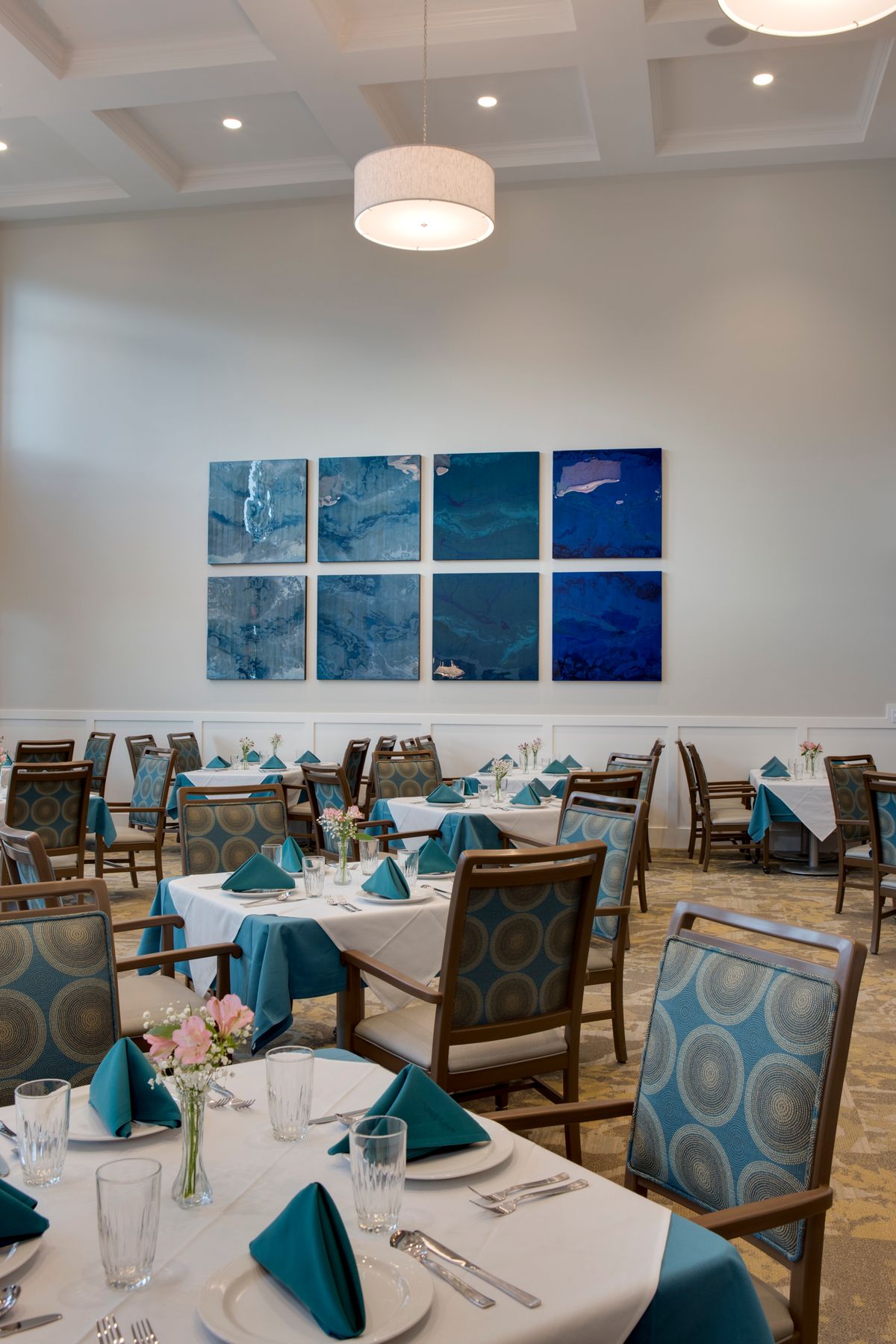 A well-lit restaurant interior with neatly arranged tables and blue-themed artwork on the wall.