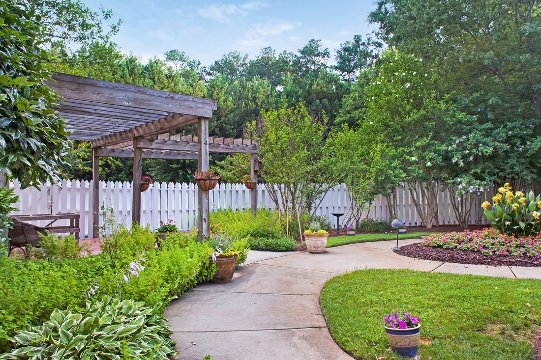 A beautifully landscaped garden featuring a pergola, lush greenery, and a winding pathway.