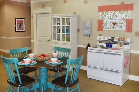 A cozy kitchen and dining area with vintage decor, featuring turquoise chairs around a round table and a white cabinet.