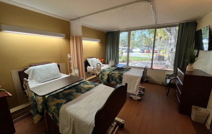 Hospital room with multiple beds and a large window providing natural light.
