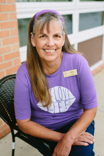 A smiling woman in a purple shirt poses for a portrait outside, radiating warmth and friendliness.
