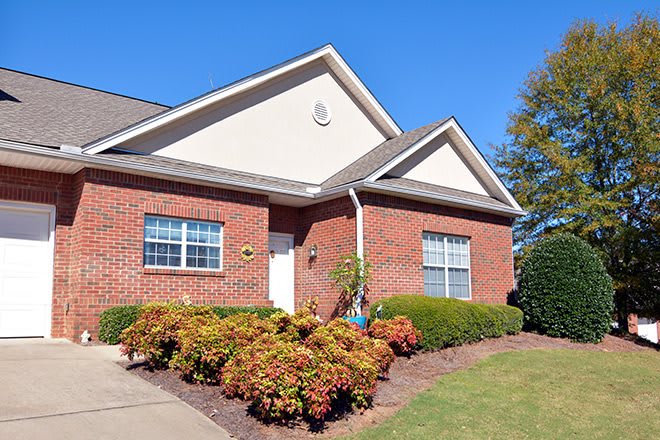 A suburban brick house with well-maintained landscaping and a clear blue sky.