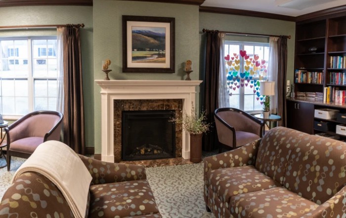 A cozy living room with a fireplace, armchairs, and a colorful stained glass window.